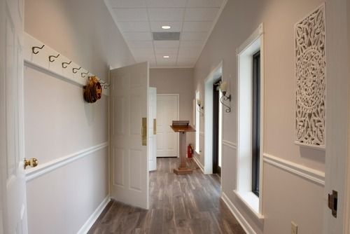 Bright hallway with white walls, wood floors, and an open door leading to a small bench at the far end.