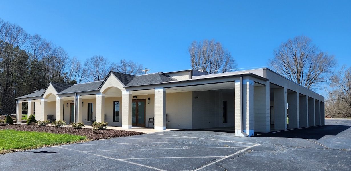 Single-story beige building with columns and a parking lot under a clear blue sky