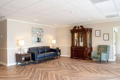 Spacious living room with blue sofa, wooden cabinet, patterned chairs, and herringbone wood floor.