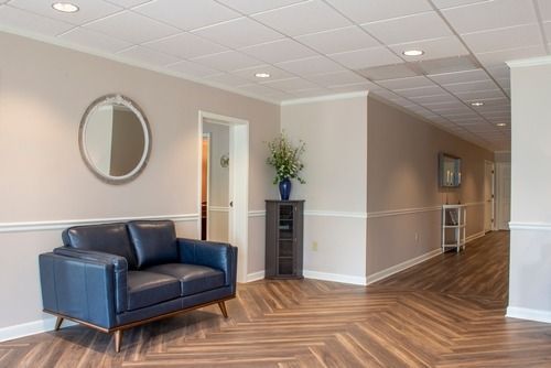 Modern office lobby with blue sofa, round mirror, potted plant, and herringbone wood floor