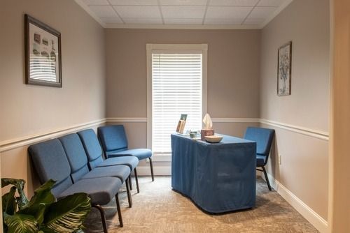 Small office waiting room with blue chairs, a desk, and a window with blinds
