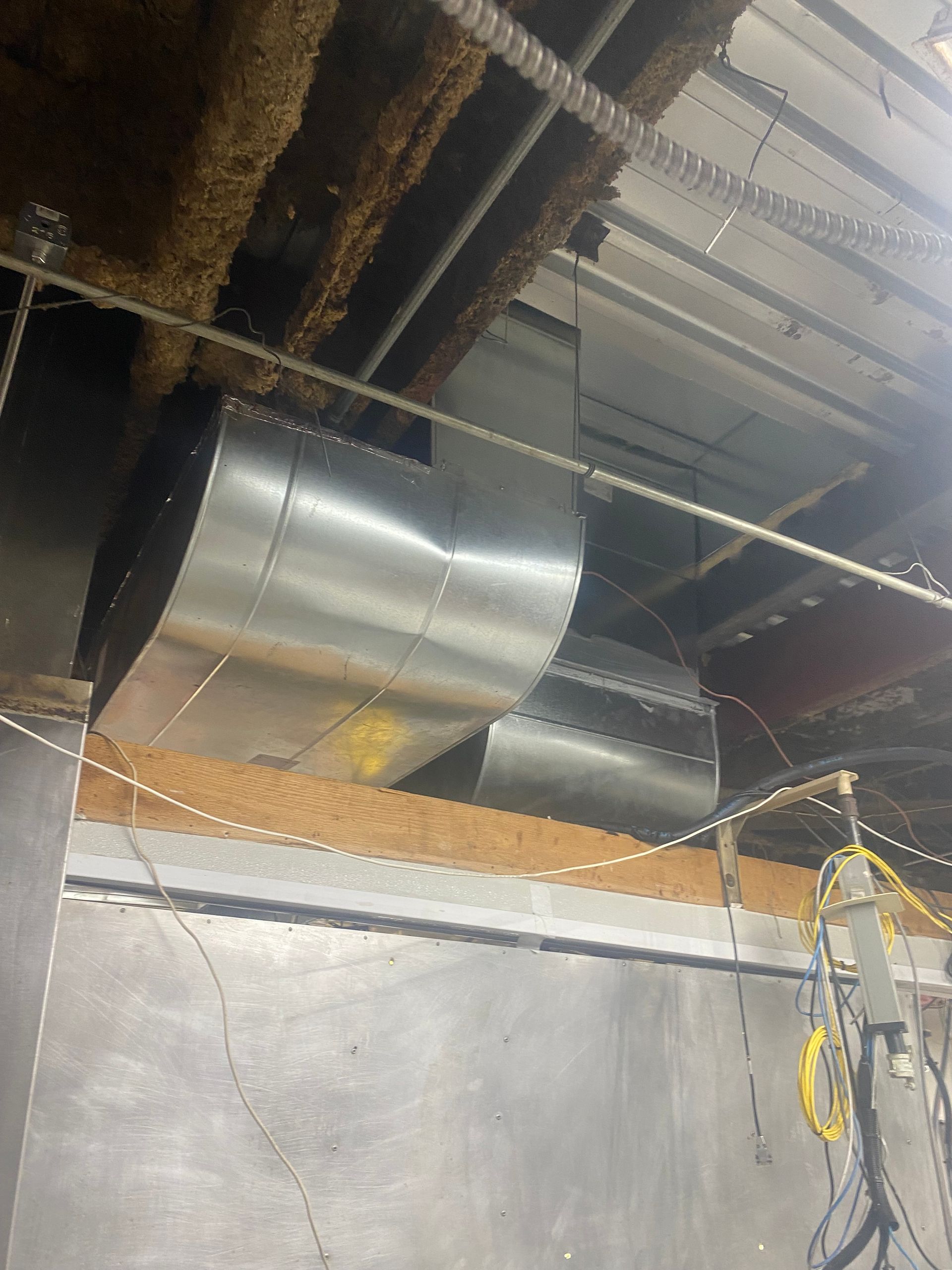Silver HVAC ducting installed in a ceiling opening above a gray wall panel.