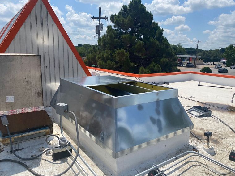 Rooftop HVAC unit on a flat roof beside a white building with red trim, under a sunny sky