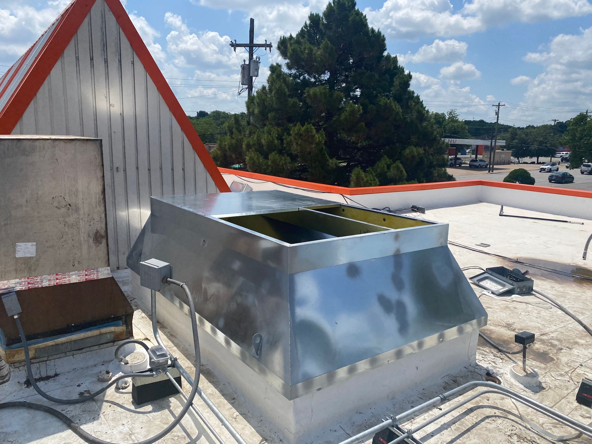Rooftop HVAC unit beside a red-trimmed building, with city street and trees in the background
