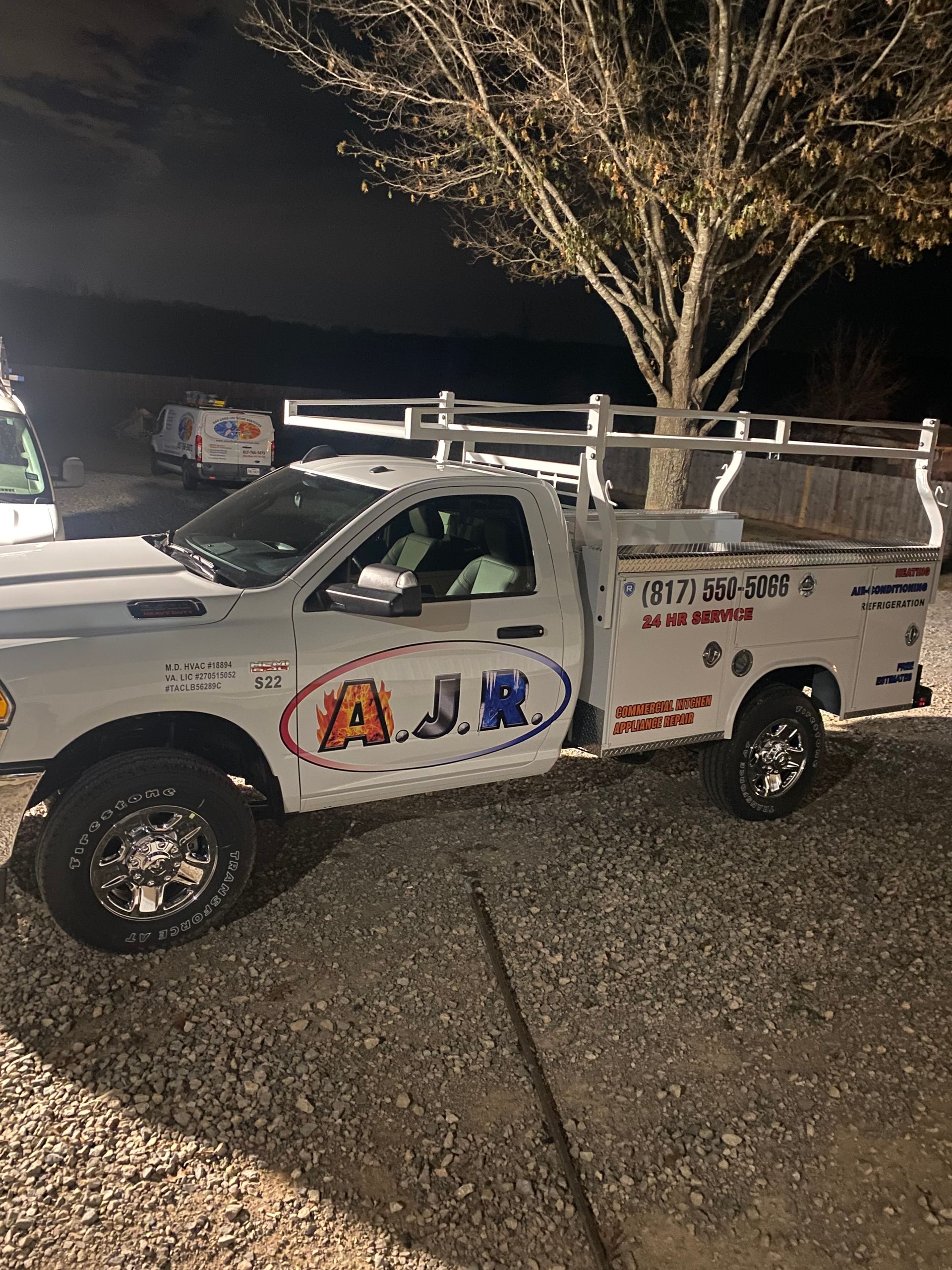 White utility pickup truck with ladder racks parked at night, lit by headlights in a dark lot