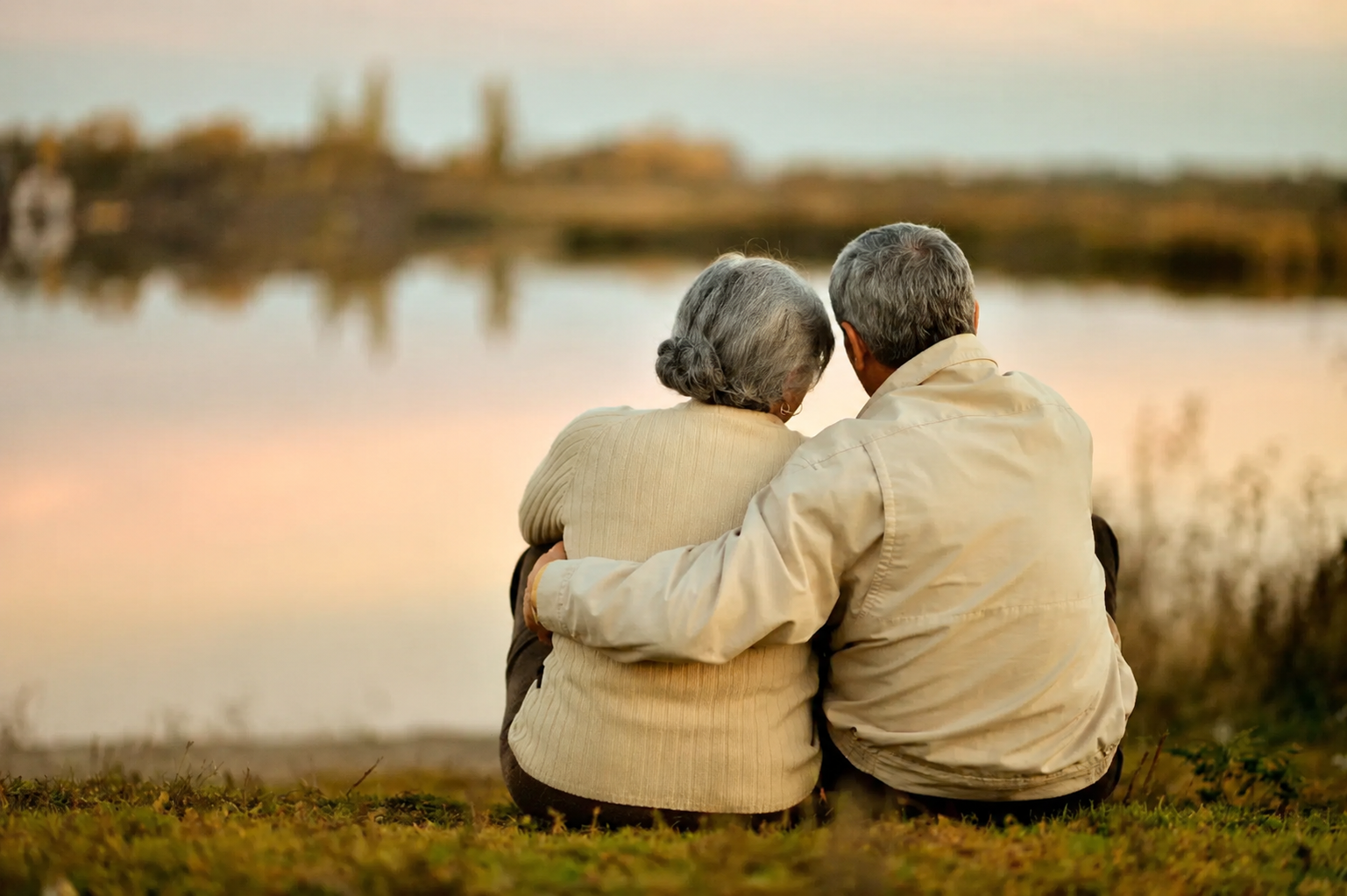 An elderly couple is sitting next to each other in front of a lake.