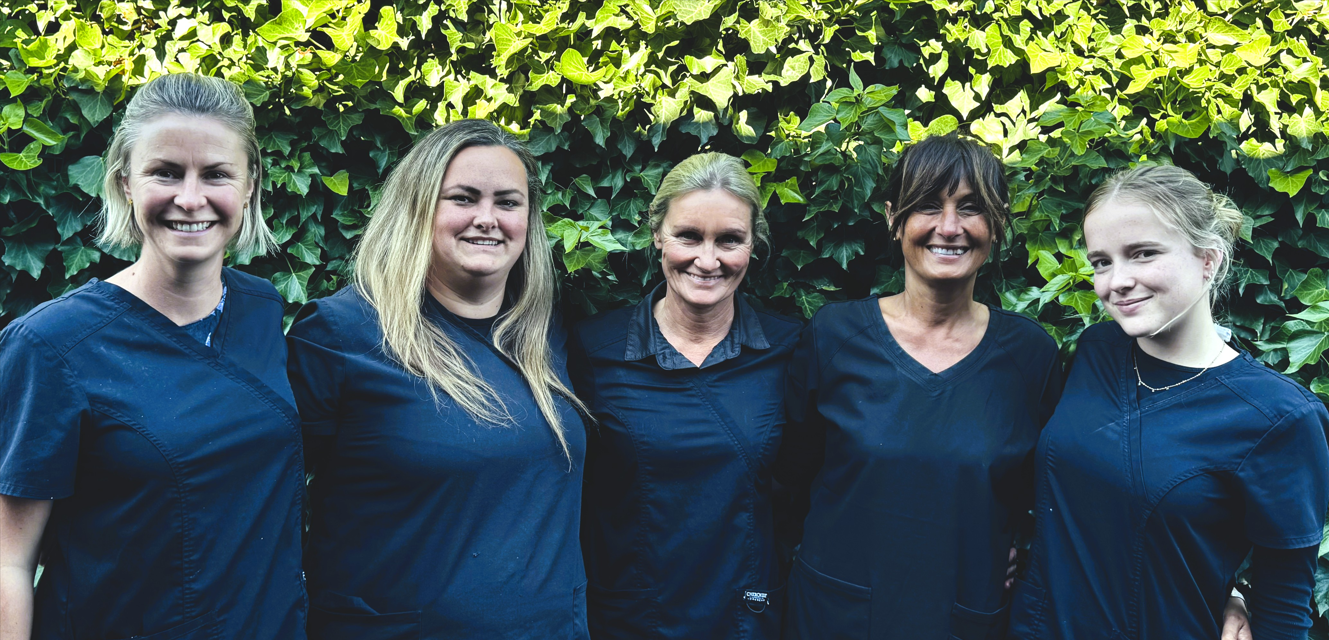 Five people standing together outdoors in navy shirts, smiling in front of green foliage
