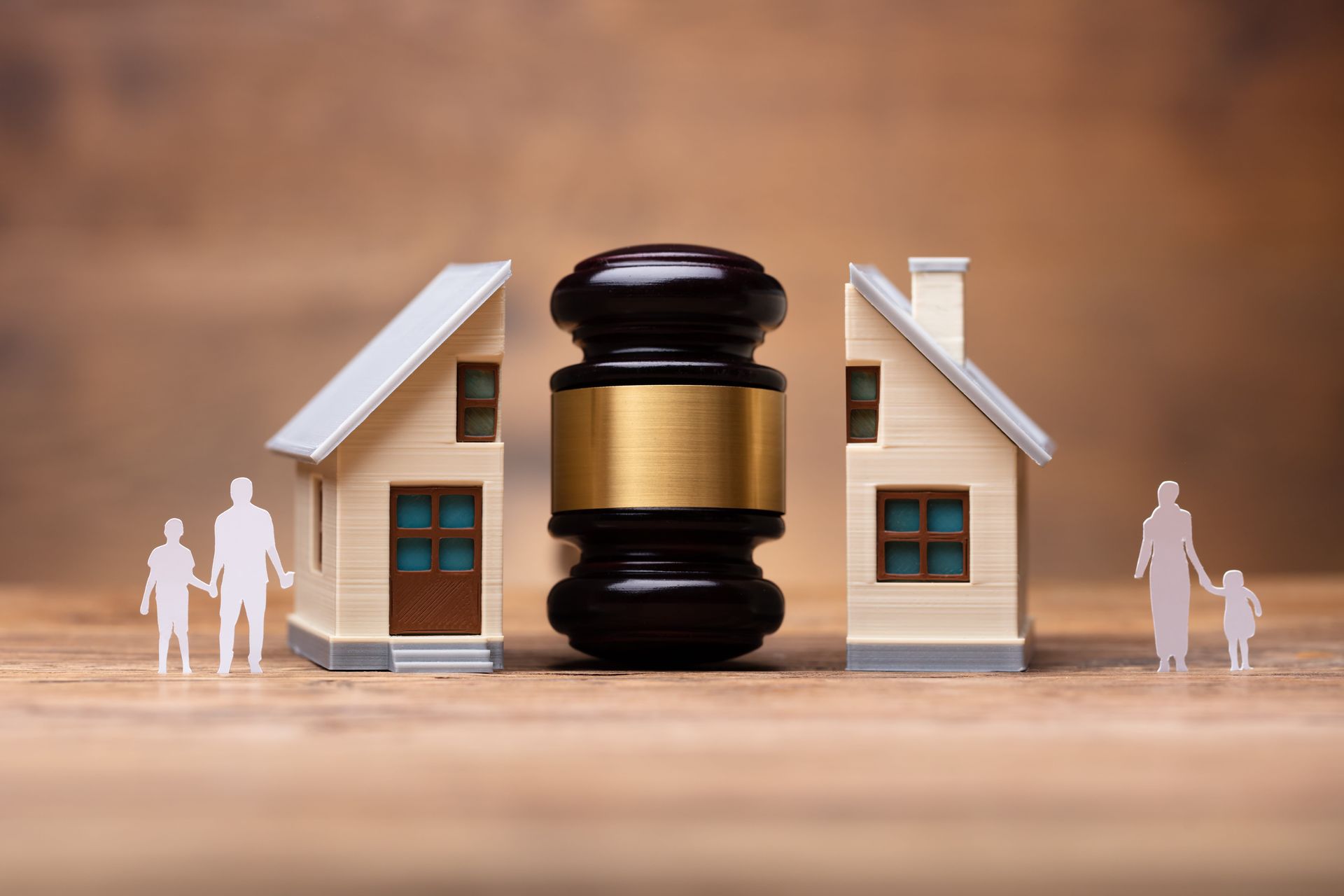 House model with a judge’s gavel between two homes and small figures, suggesting a property dispute
