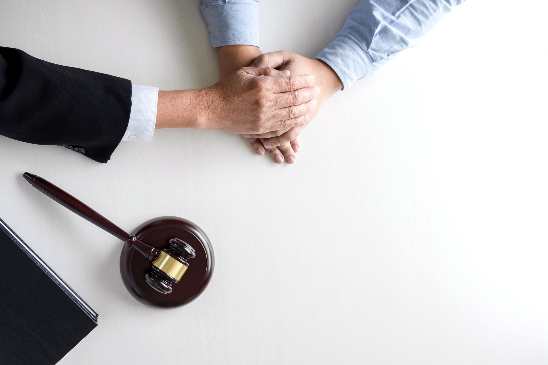 Hands clasped on a white surface next to a gavel and documents, suggesting legal support or counsel.