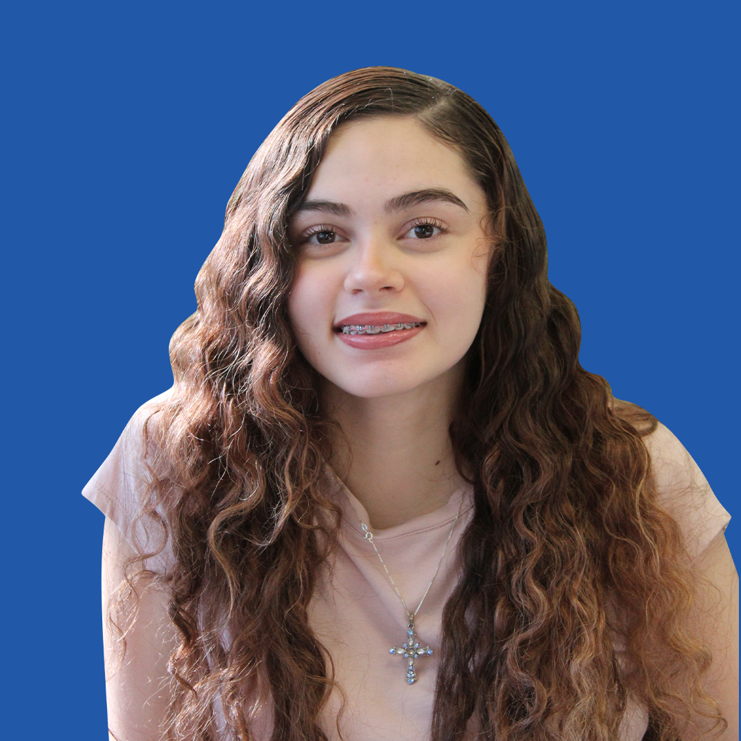 A young woman with long curly hair and braces on her teeth is standing in front of a blue background.