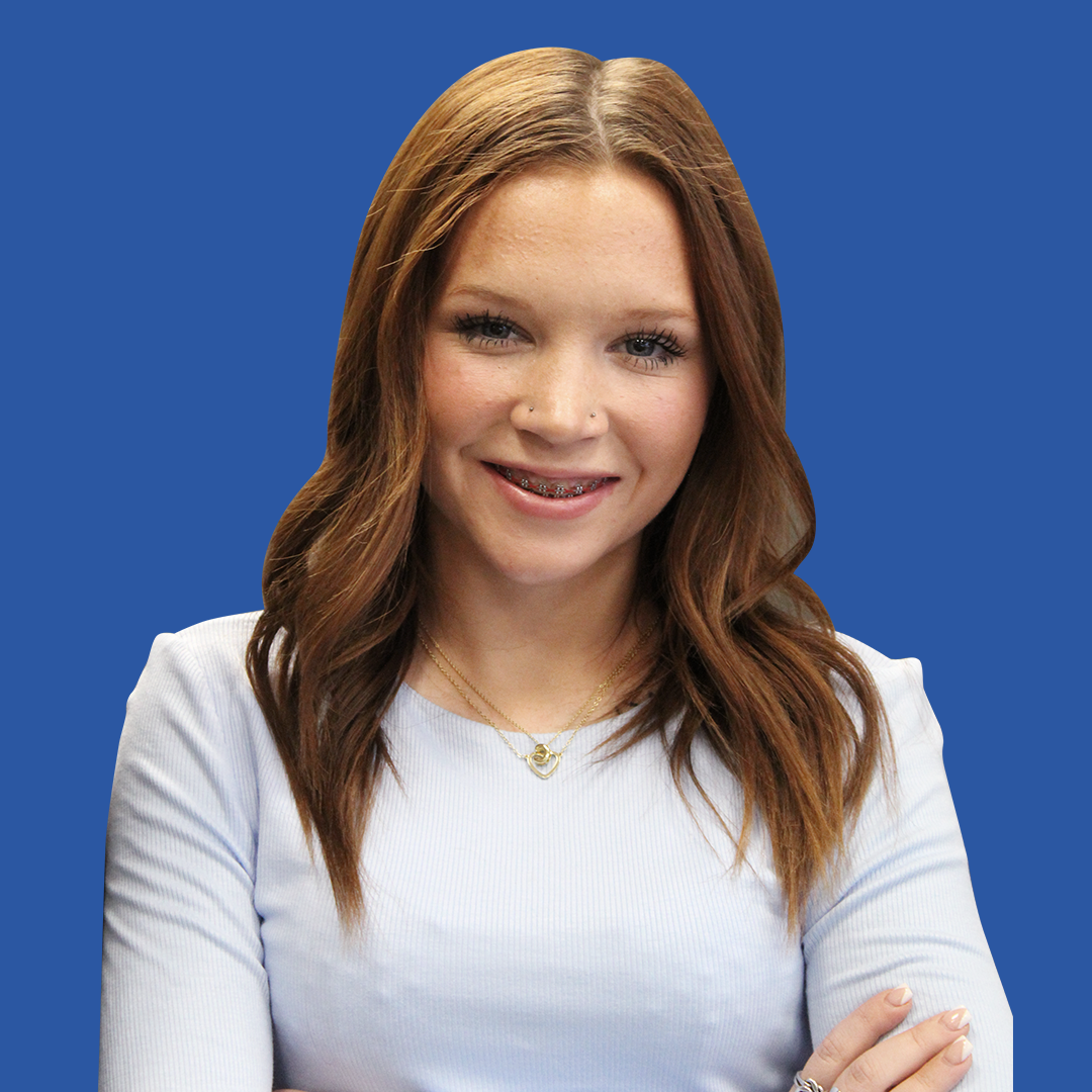 A woman in a white shirt is smiling with her arms crossed
