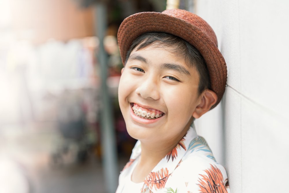 A young boy wearing a hat and clear ceramic braces is smiling.
