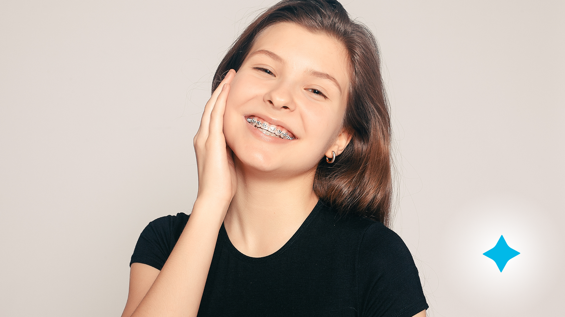 A young girl with braces on her teeth is smiling and touching her face.