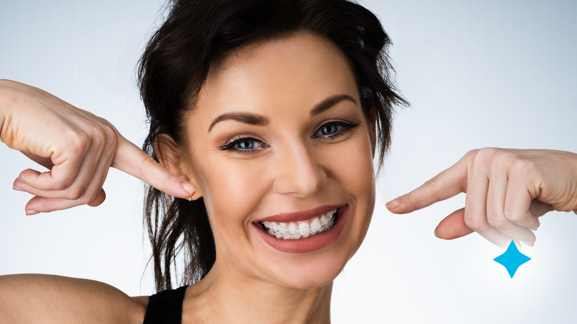 A woman is smiling and pointing at her teeth.