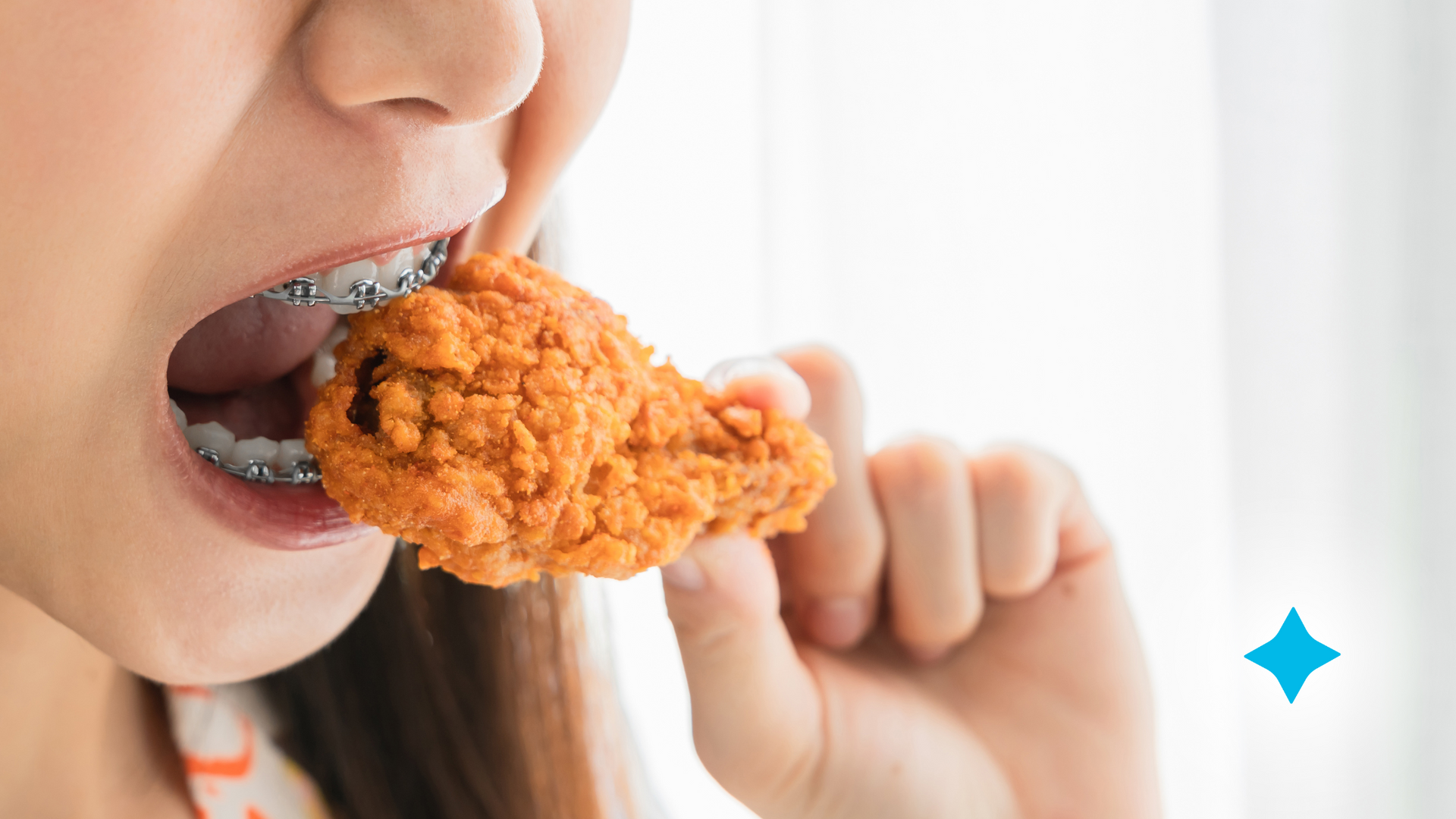 A woman with braces is eating a piece of fried chicken.