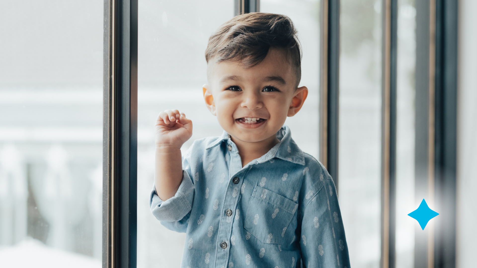 A young boy is standing in front of a window and smiling.