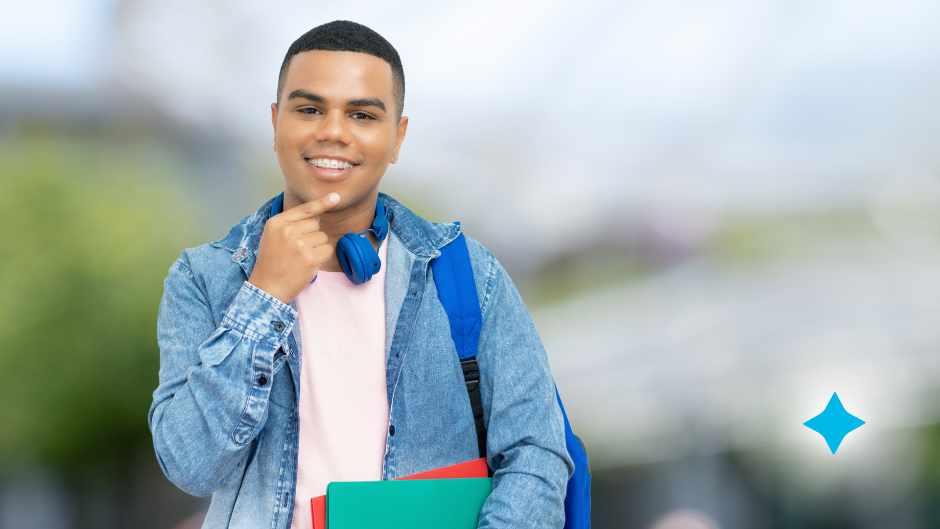 A young man wearing headphones and a backpack is holding books and smiling.