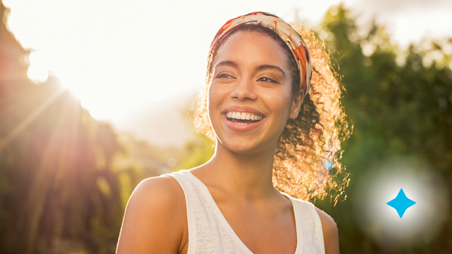 A woman wearing a headband is smiling in the sunlight.
