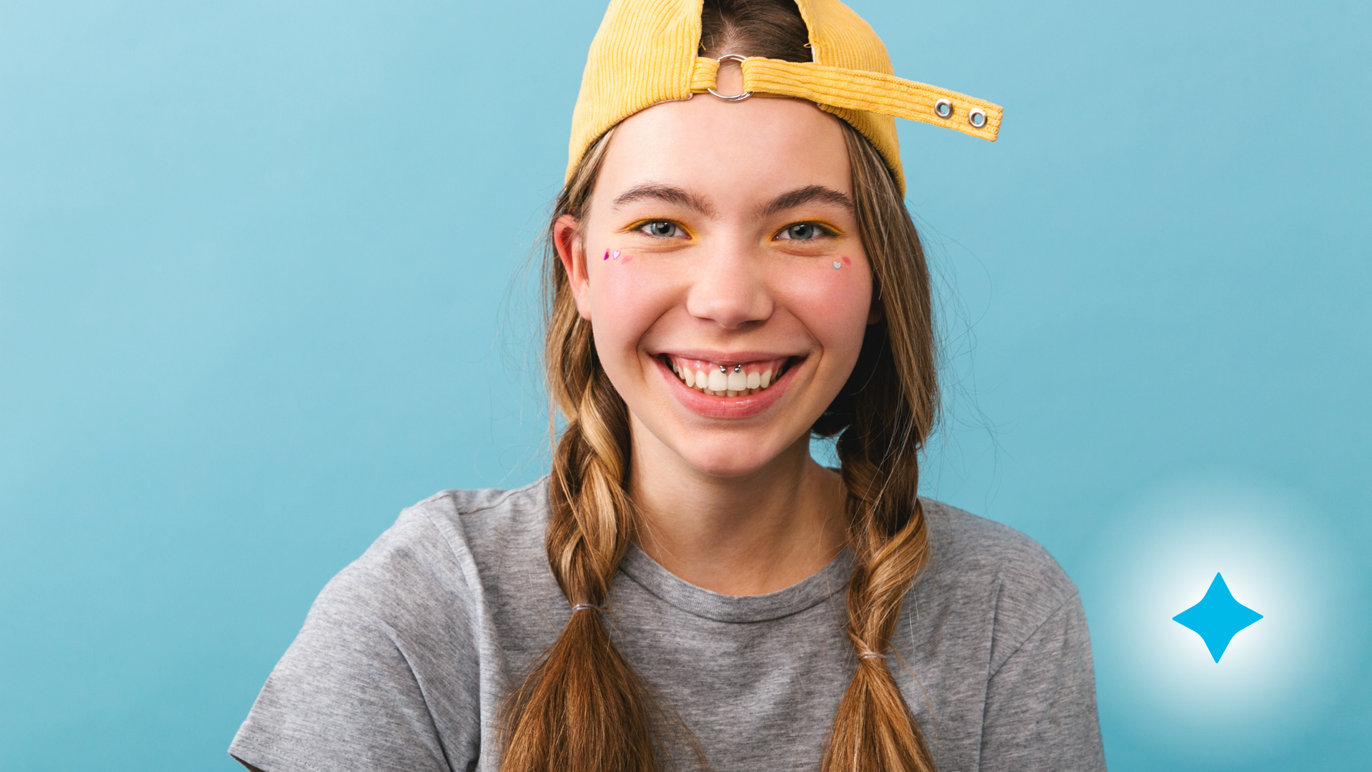 A young woman wearing a baseball cap and braids is smiling.