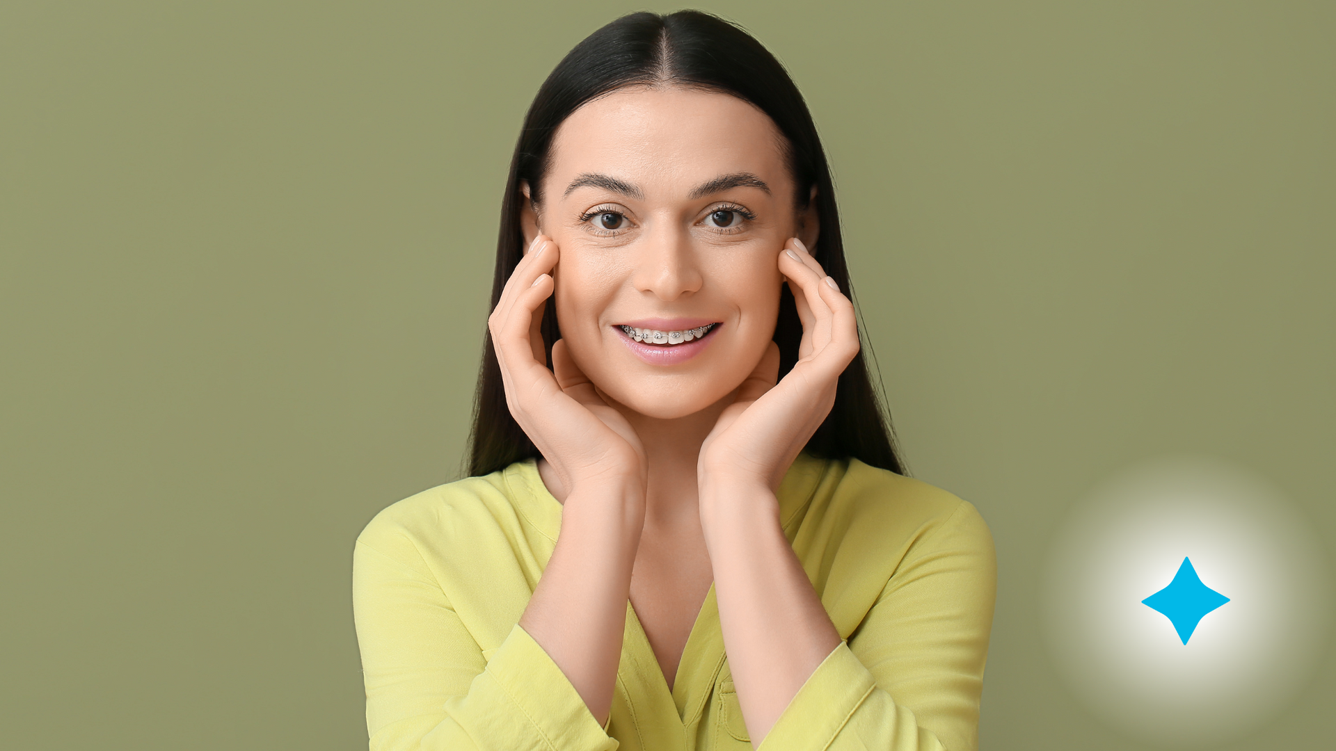 A woman with braces on her teeth is smiling and touching her face.
