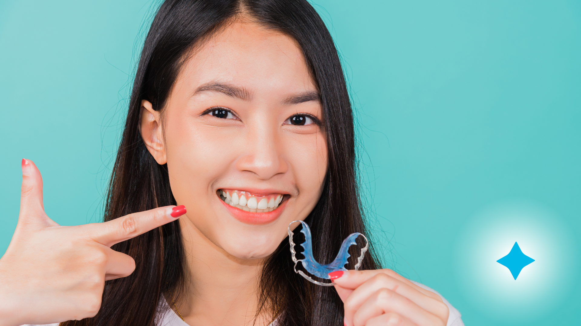 A woman is smiling and pointing at her teeth while holding a retainer.