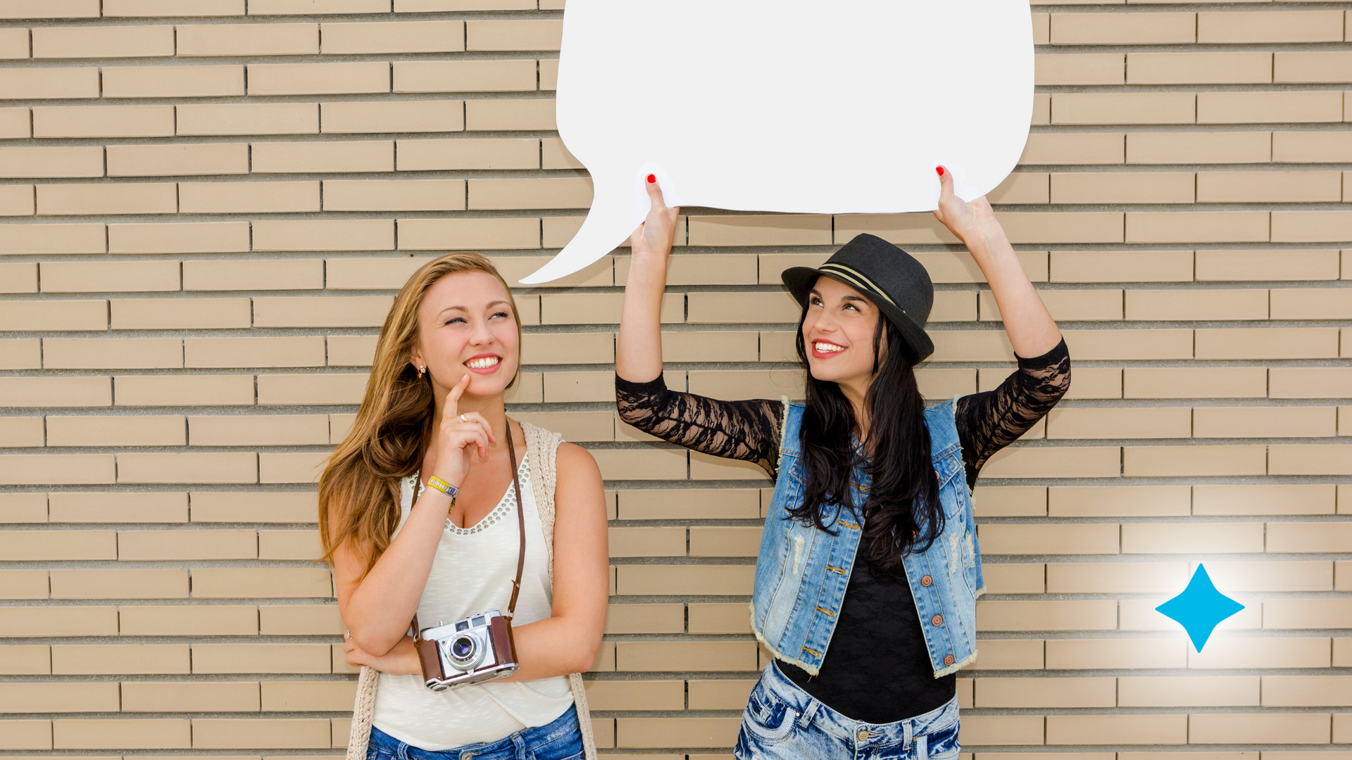 Two women are standing in front of a brick wall holding a speech bubble.