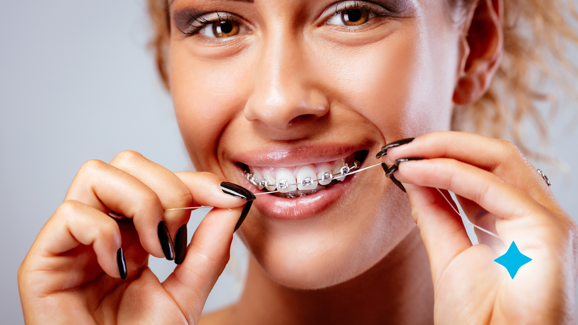 A woman is smiling while flossing her teeth and wearing braces on her teeth.