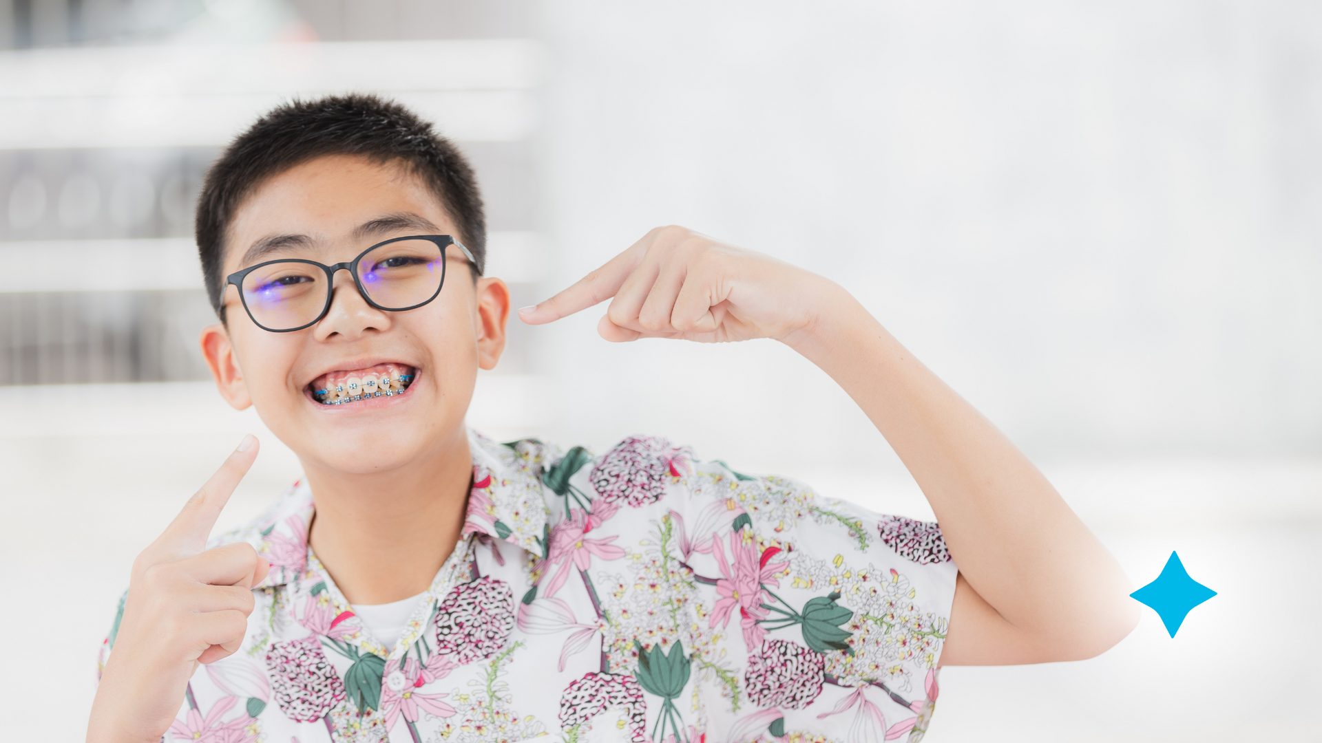 A young boy wearing glasses and braces is pointing at his teeth.