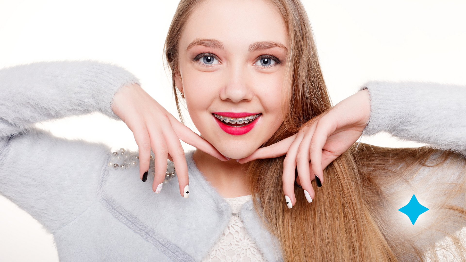 A young woman with braces on her teeth is smiling and touching her face.