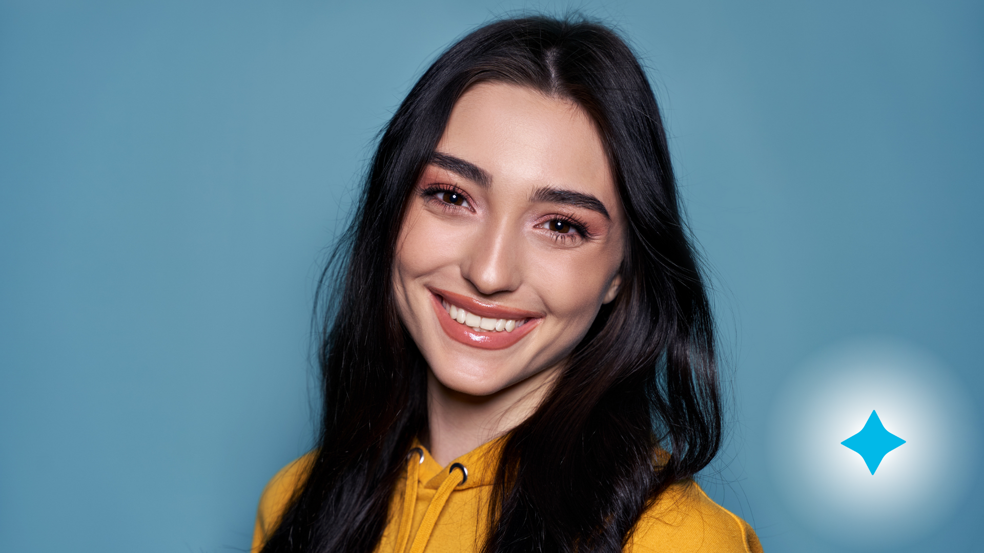 A woman in a yellow shirt is smiling in front of a blue background.