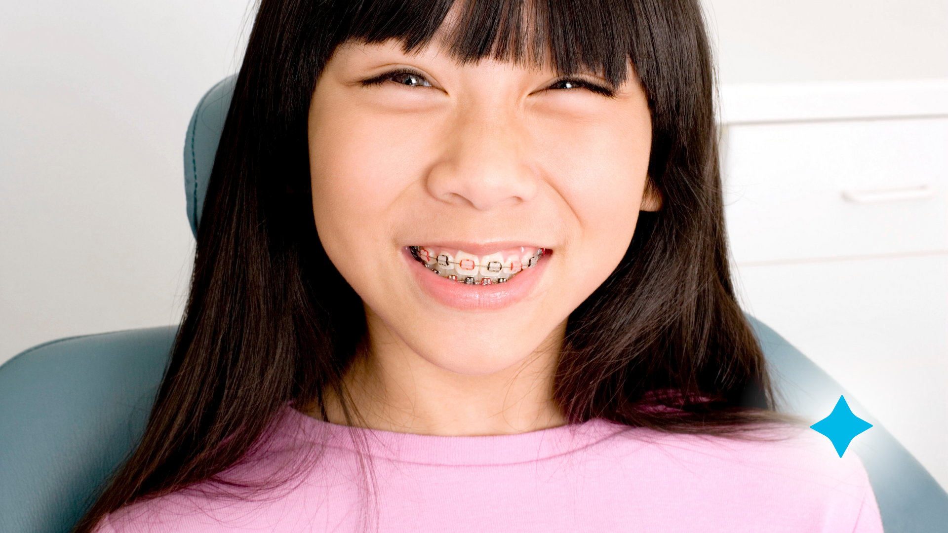 A young girl with braces is smiling while sitting in a dental chair.
