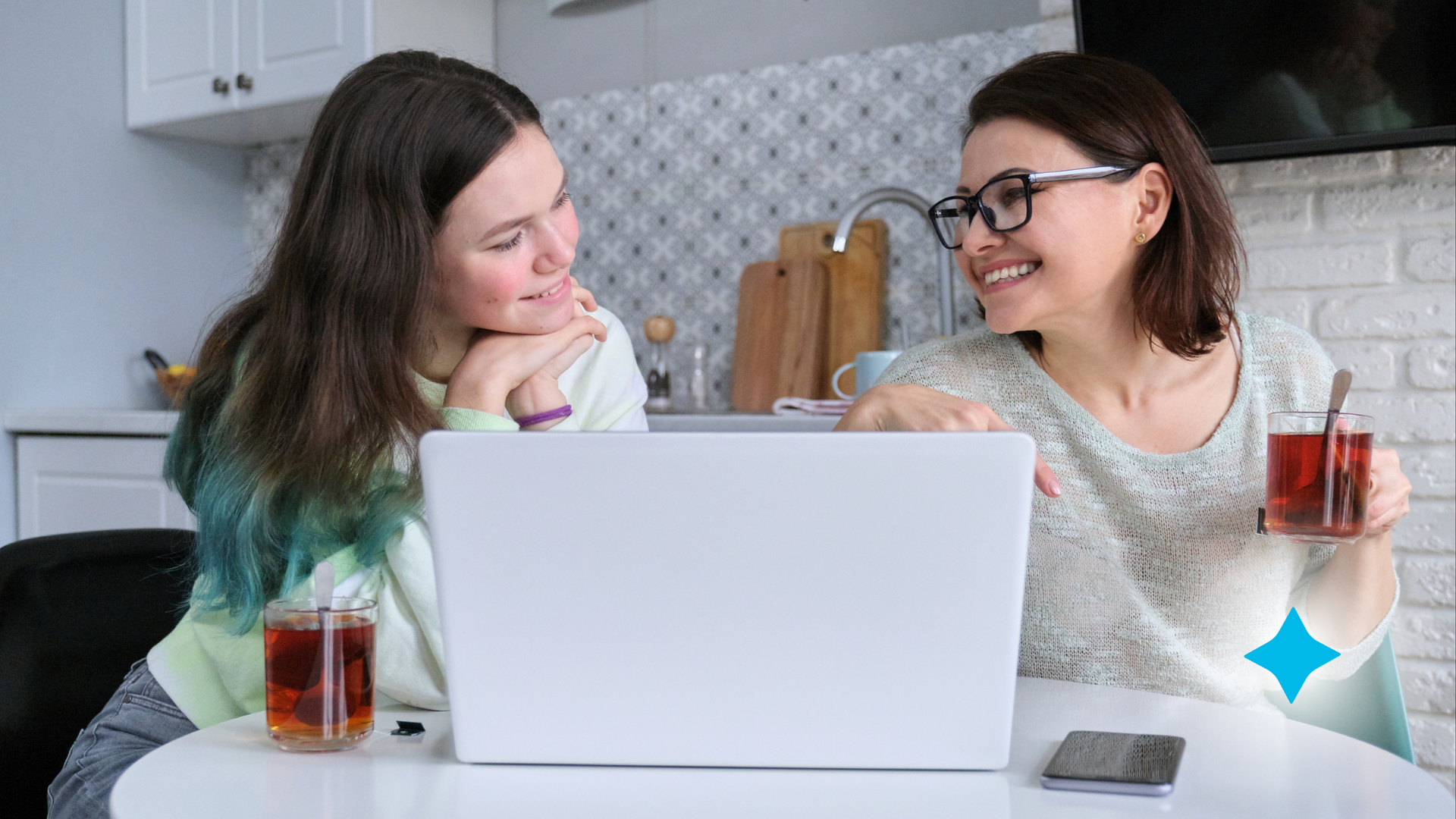 Two women are sitting at a table looking at a laptop computer.