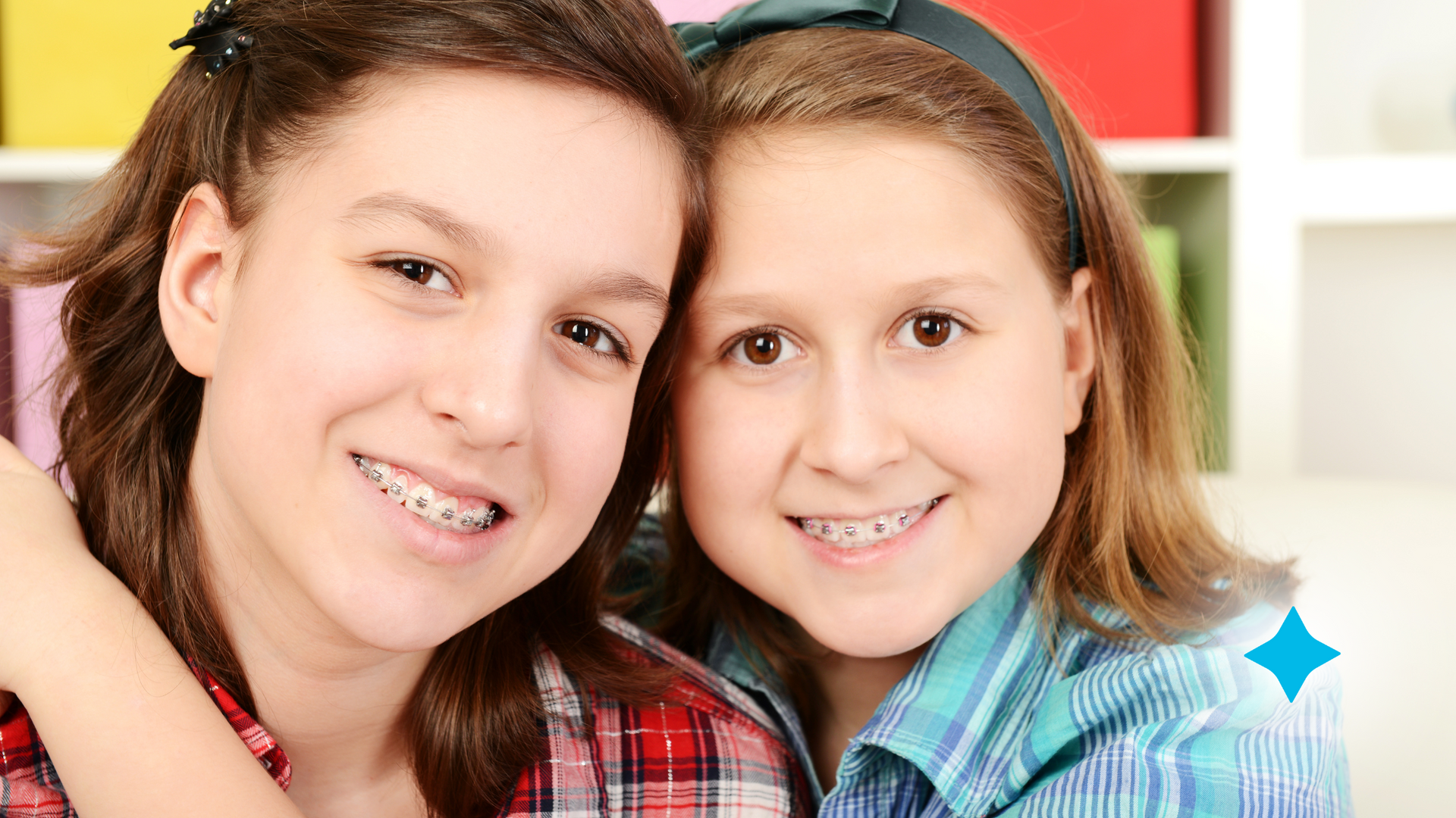 Two young girls with braces are hugging each other and smiling for the camera.