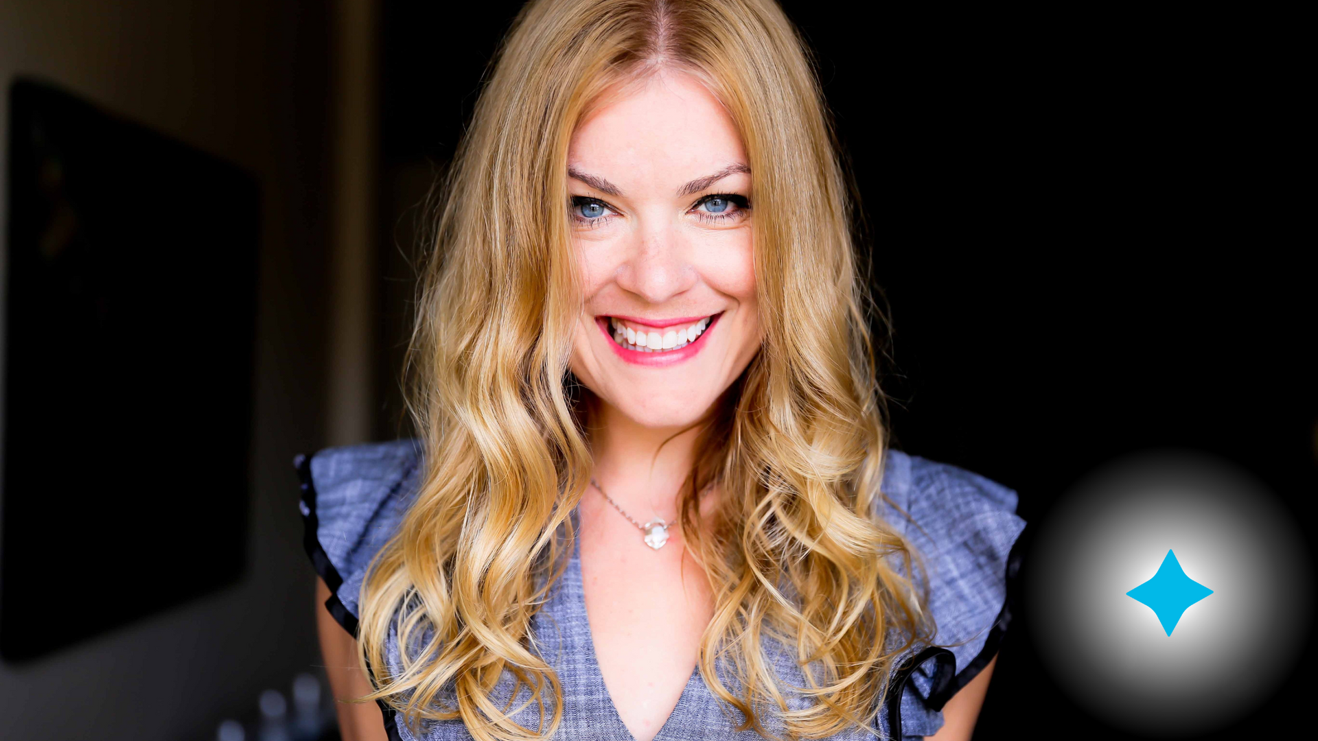 A woman with long blonde hair is smiling and wearing a necklace.