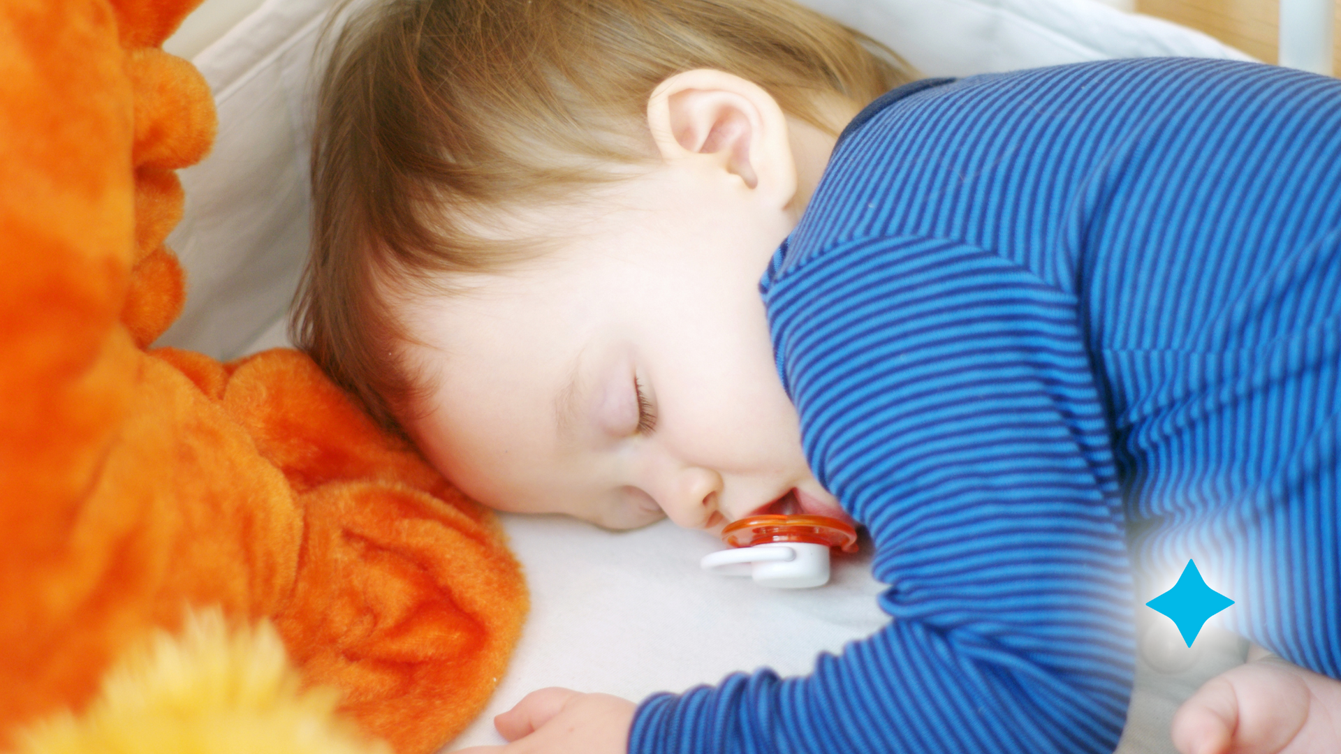 A baby is sleeping in a crib with a pacifier in his mouth.