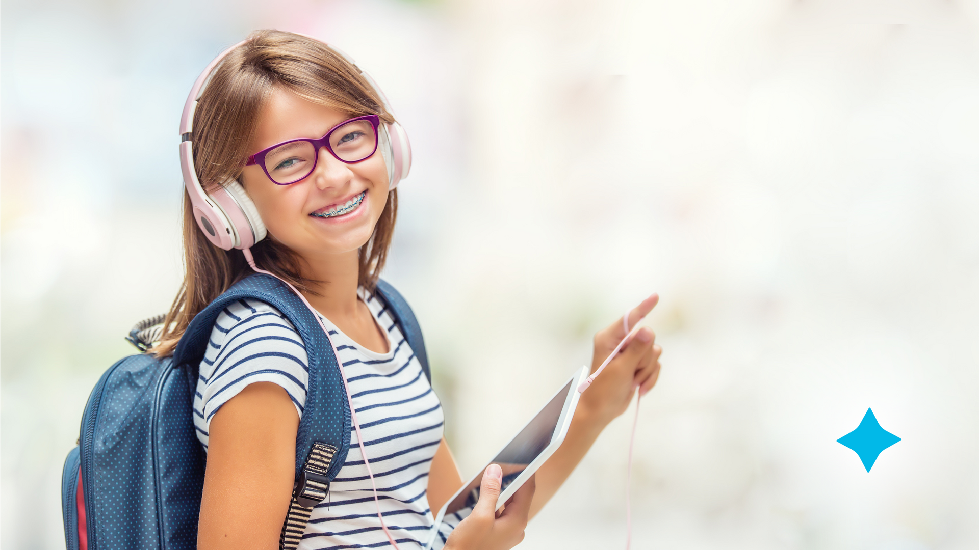 A young girl wearing headphones and glasses is holding a tablet.