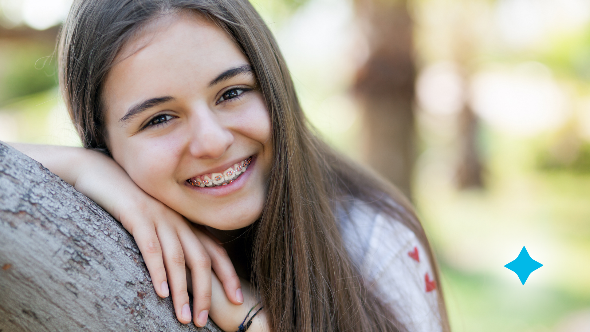 A young girl with braces is leaning on a tree branch.