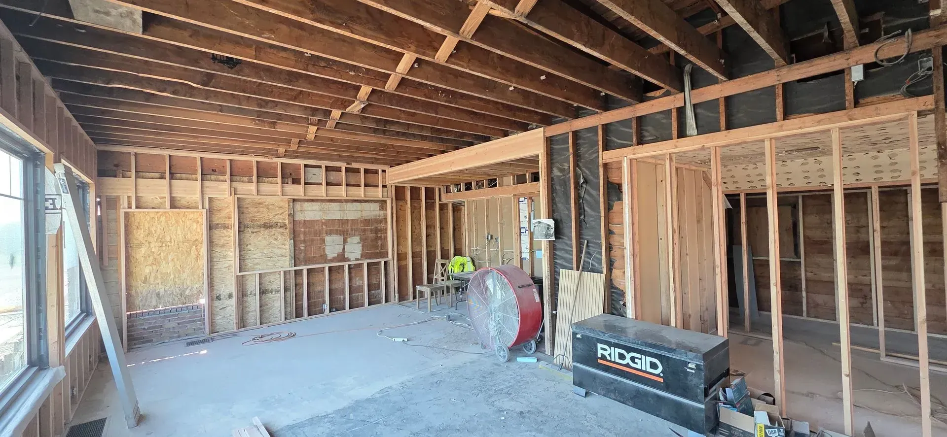 Interior of a house under construction with exposed framing, insulation, and a worker in a yellow vest near tools.