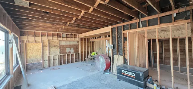 Interior of a framed house under construction with exposed studs, unfinished walls, and construction tools on the floor