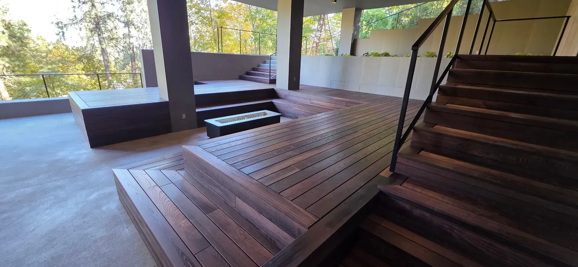 Wooden deck walkway and stairs under a covered patio, with trees visible beyond the railing.