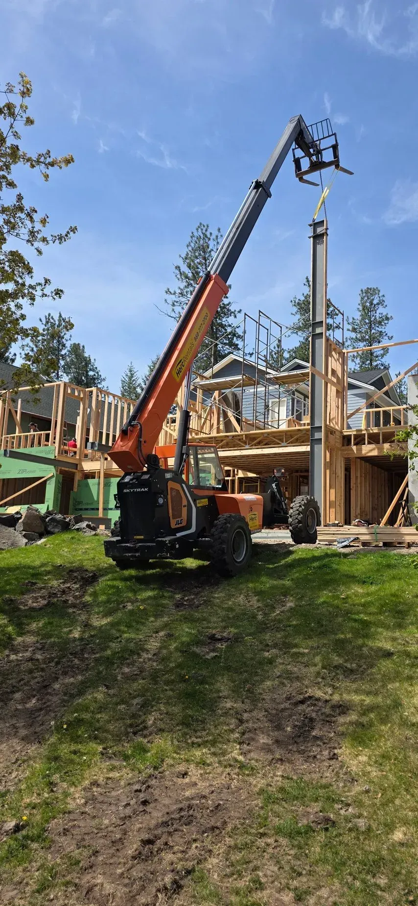 Orange construction crane lifting a prefabricated house frame at a building site under blue sky