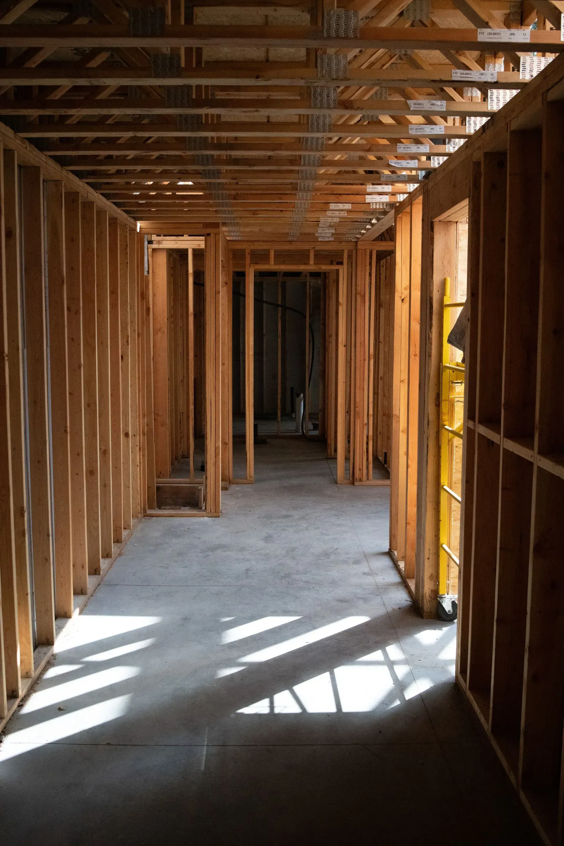 Unfinished wooden hallway with exposed studs and beams, sunlight casting shadows on the floor.