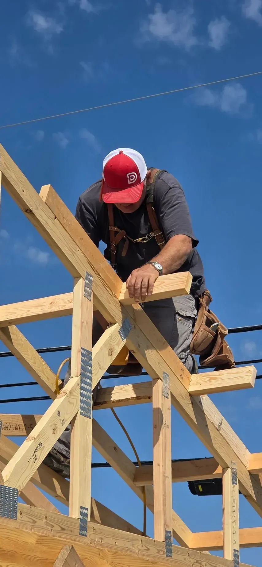 Construction worker in a red cap securing wooden roof framing against a blue sky