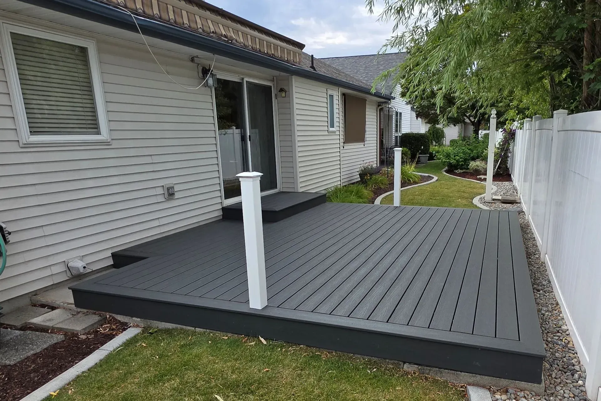 Backyard deck beside a house with gray boards, white posts, and a white fence.