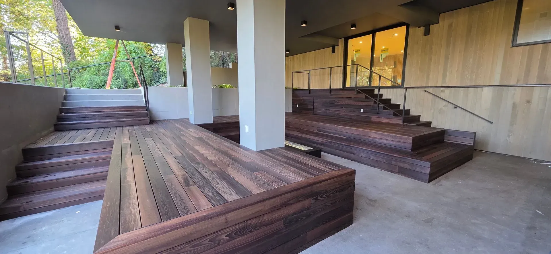 Empty outdoor amphitheater with tiered wooden benches and stairs under a covered patio