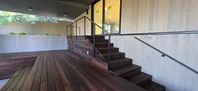 Outdoor deck with wooden stairs and a metal handrail beside a white wall