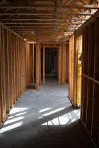 Unfinished wooden hallway with exposed framing and sunlight streaming through open wall studs.