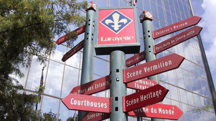 Signpost in Lafayette, Louisiana, with directions to local attractions, featuring a fleur-de-lis.