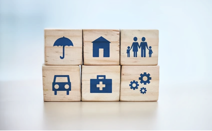 Wooden blocks with insurance icons: umbrella, house, family, car, medical bag, gears.