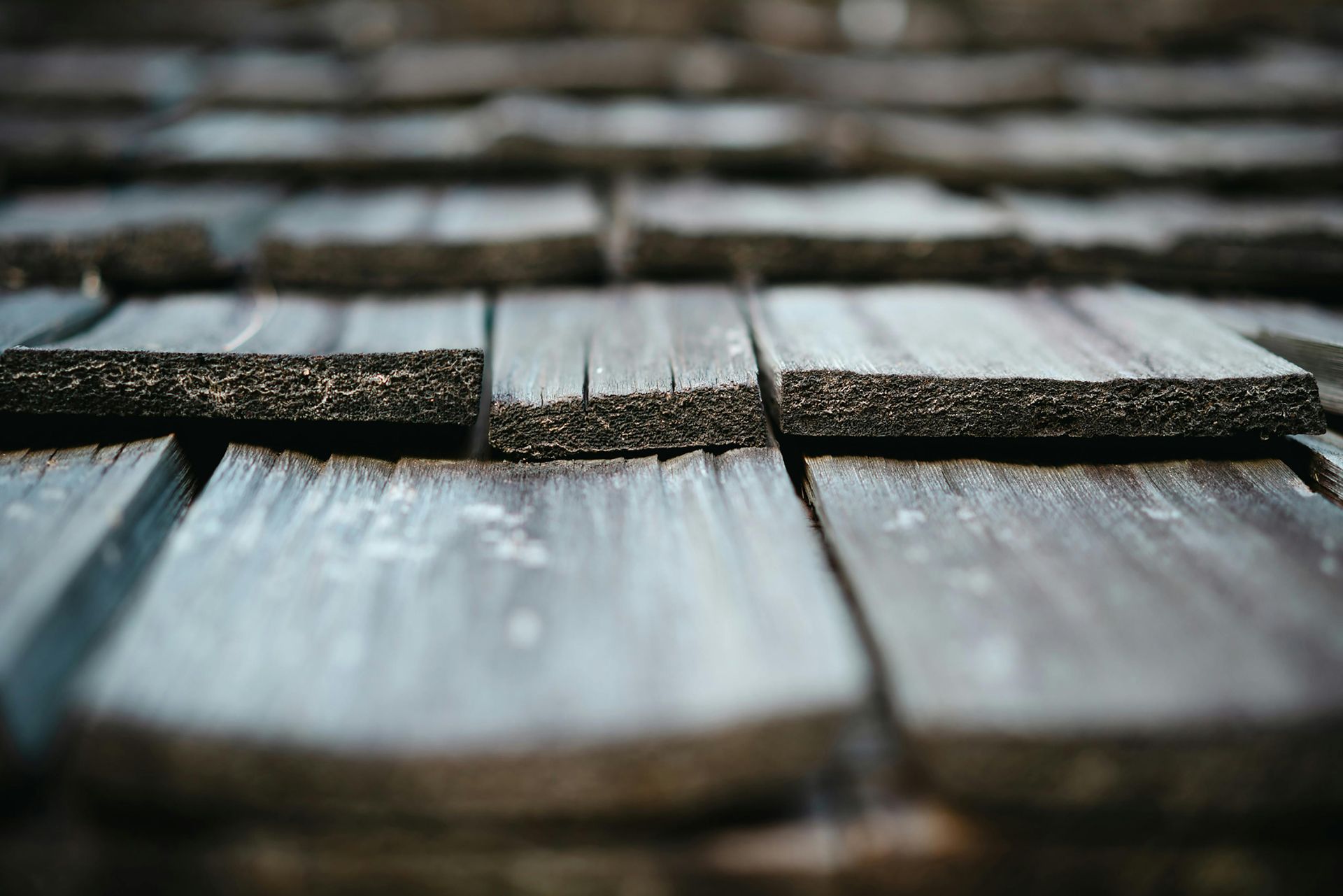 Close-up of weathered wooden shingles with blurred white frost or snow in the foreground